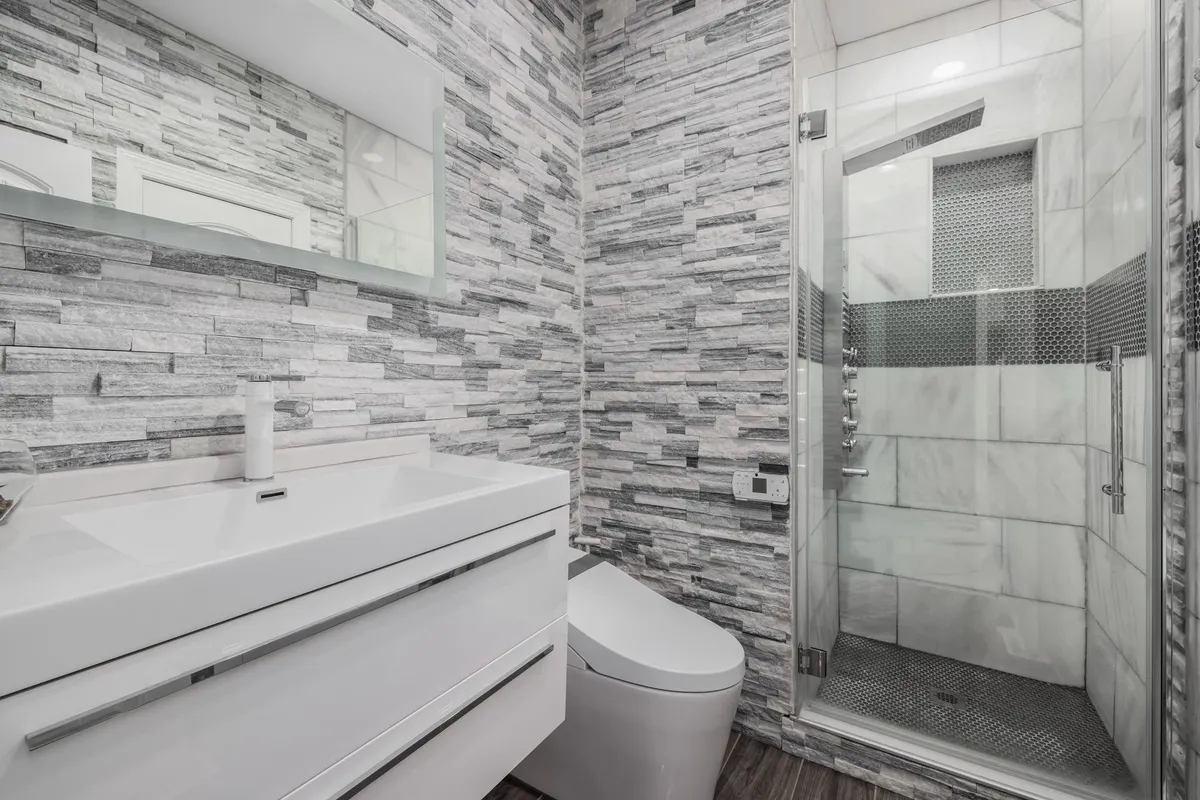 A modern bathroom with a glass shower, stone walls, and a sleek white vanity, showcasing custom design options.